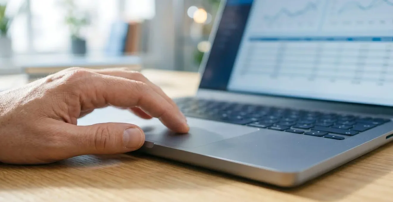 Extreme Nahaufnahme einer Hand auf einem modernen Laptop-Trackpad mit unscharfem Bildschirm im Hintergrund, der eine Vergleichsoberfläche zeigt