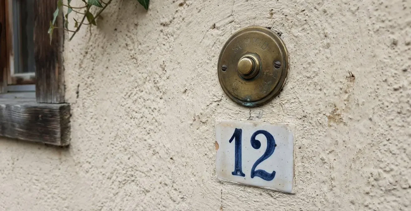 Nahaufnahme einer typischen Schweizer Hausfassade mit messingfarbenem Klingelschild und blauer Hausnummer auf hellem Putz